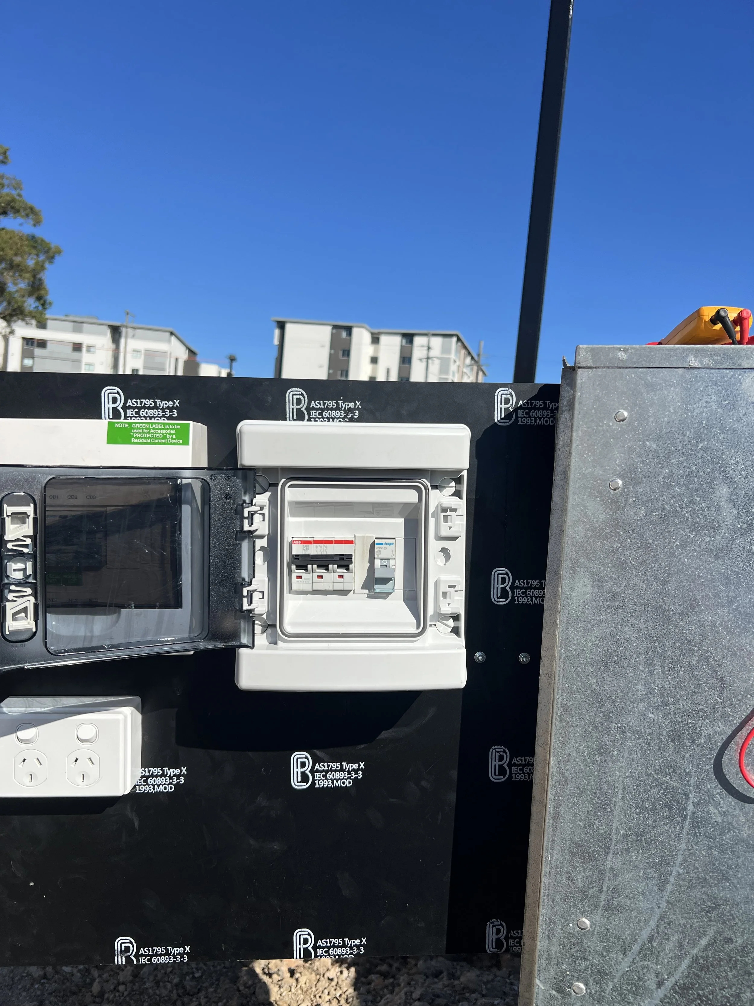 Electrical breaker box, power outlets, and electrical wiring on an outdoor electrical box with a clear blue sky in the background.