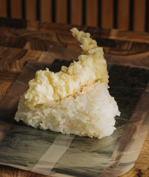 A piece of tempura battered fried fish placed on a black rectangular plate on a wooden table.