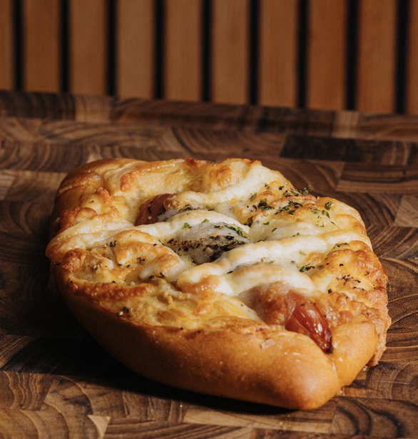 Close-up of a savory stuffed bread with cheese, herbs, and tomato on a wooden surface.
