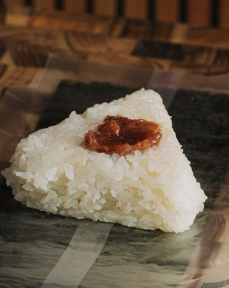 A rice ball with a filling of pickled plum paste in the center, on a piece of dark seaweed wrap.