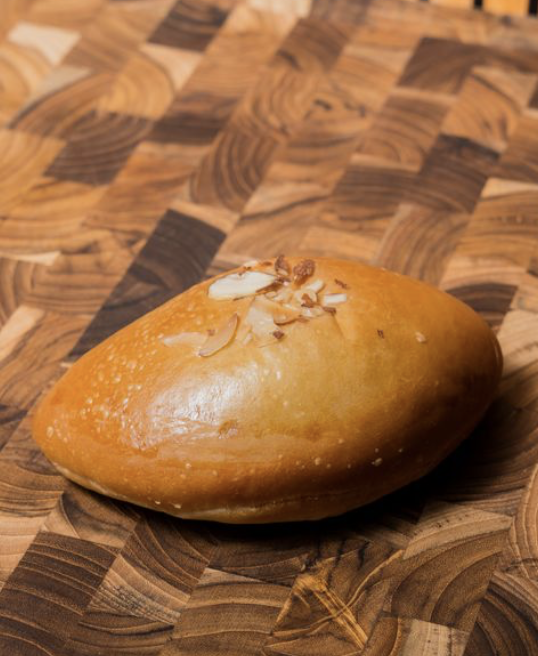 A golden brown chocolate custard bread topped with sliced almonds on a wooden surface.