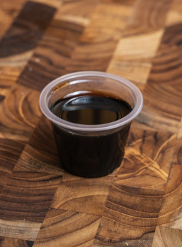 A small plastic cup filled with black eel sauce on a wooden surface.