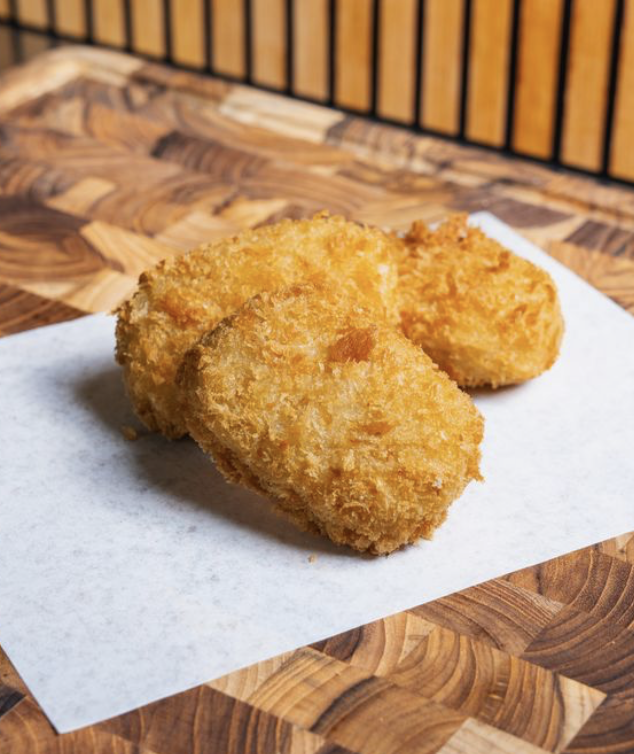Three pieces of fried croquette on white paper, placed on a wooden surface with a black and yellow striped background.