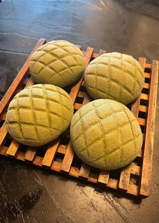 Four round matcha-flavored bread rolls with a grid pattern on top, on a wooden tray.