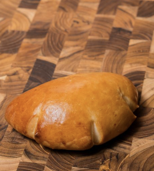 A freshly baked custard bread with a golden-brown crust on a patterned wooden surface.