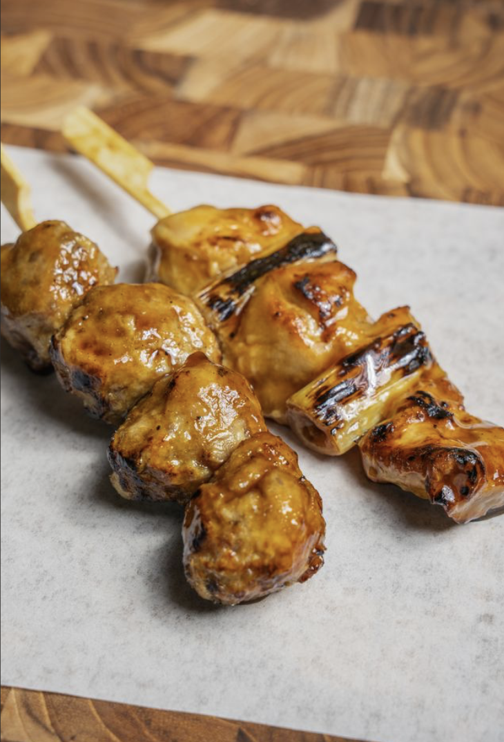 Close-up of grilled skewers with glazed meat, placed on parchment paper on a wooden surface.