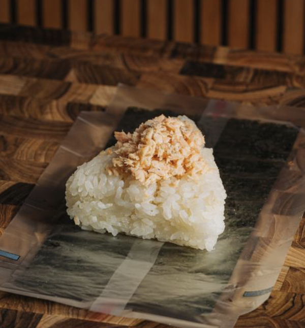 Rice ball with shredded cooked chicken on top, placed on plastic wrap on a wooden surface.