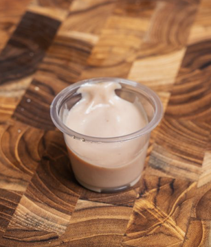 Small clear plastic cup of aurora sauce on wooden surface.