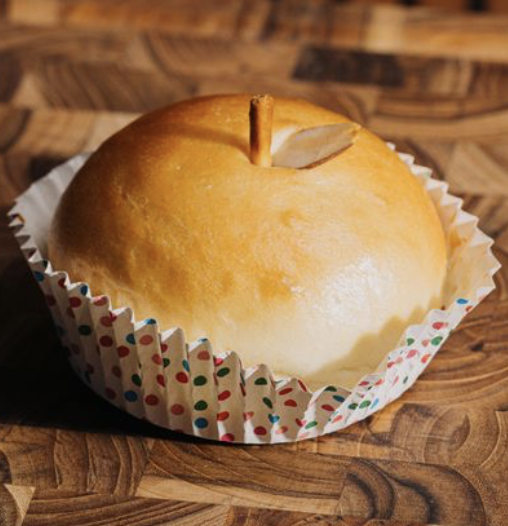 Baked apple shaped bread in a paper cupcake liner on a wooden surface.