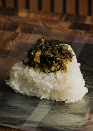 A rice ball topped with pickled greens on a plate.