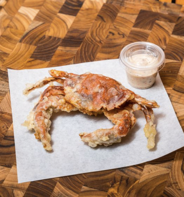 Fried crab with dipping sauce on a white paper sheet on a wooden table.