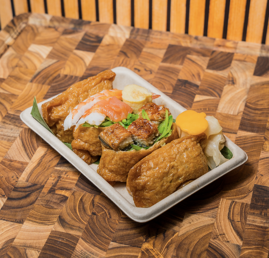 A rectangular plate with assorted Japanese sushi , including tofu, sushi with shrimp and fish, pickled ginger, on a wooden table.