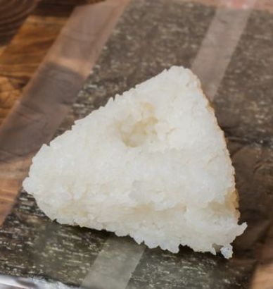 A close-up of a triangular piece of white rice called rice ball on a wooden surface.