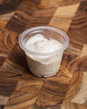 A small plastic cup of spicy mayo on a wooden surface.