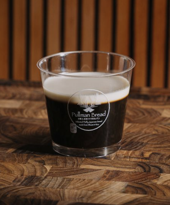 A clear plastic cup of dark coffee jelly with white milk layer on a wooden table, with a wooden slat background.