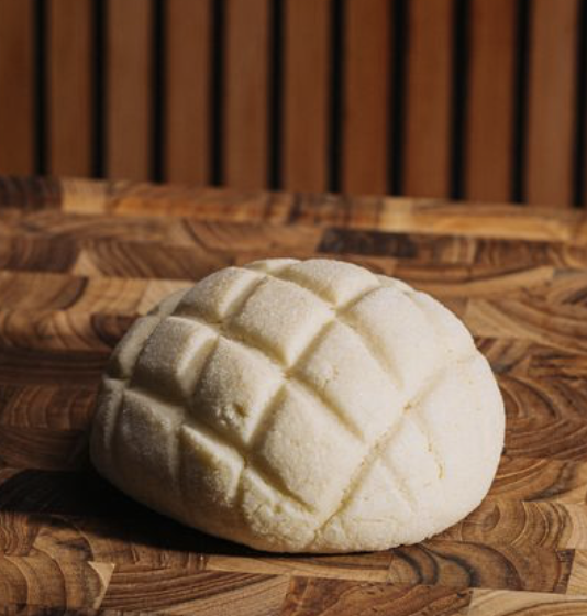 A piece of bread with a crosshatch pattern on top, placed on a wooden surface.