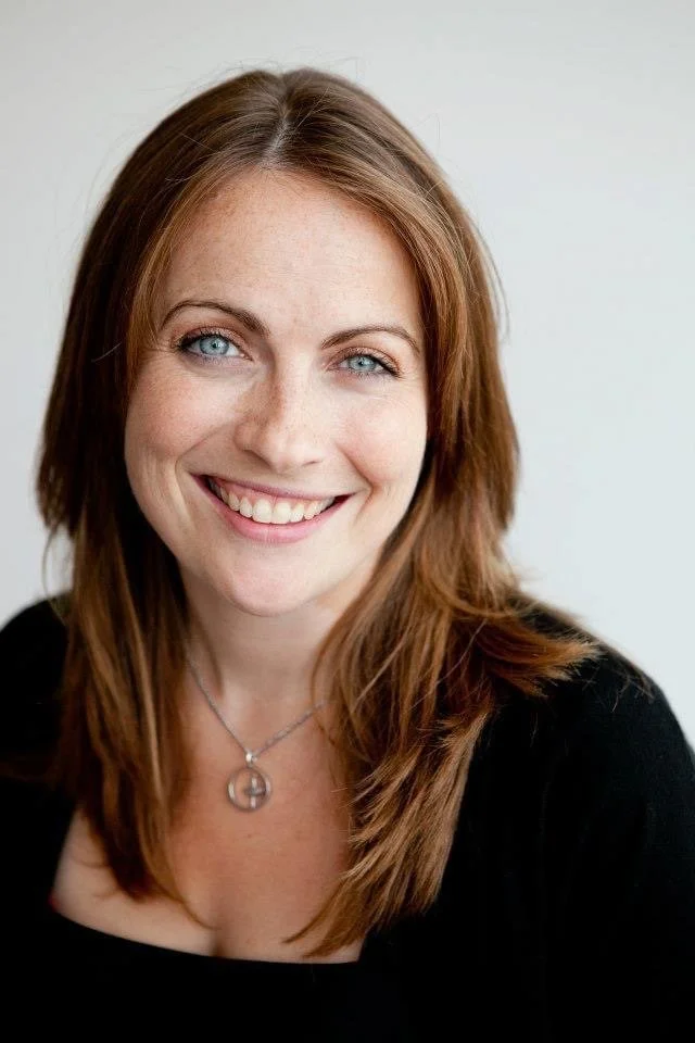 Madeline Binsfrahm smiling with blue eyes, parted auburn hair and a black top