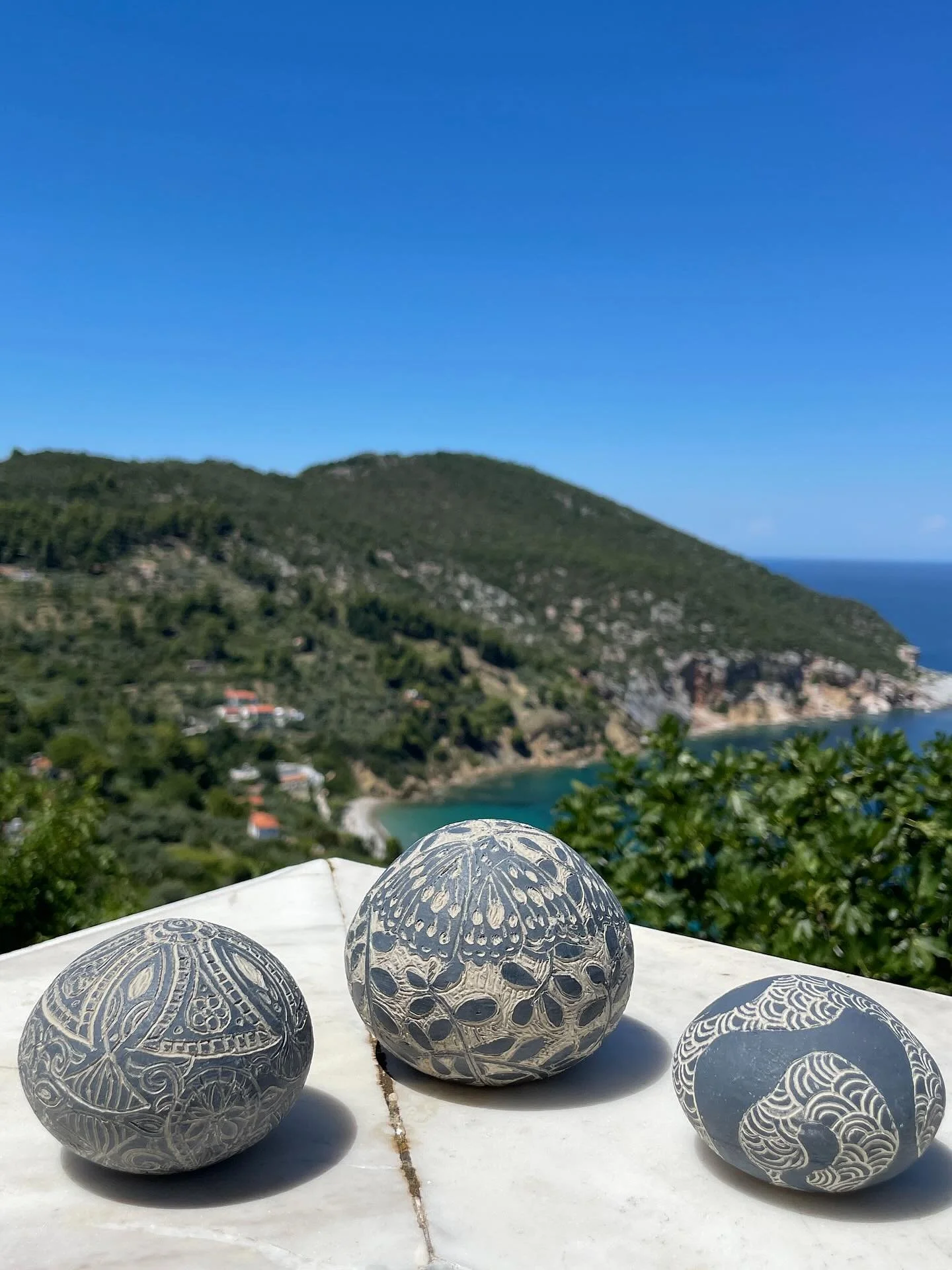 During my time at SkopArt, I have been creating a small series of works inspired by the smooth pebbles scattered along the beaches of Skopelos. The intricate sgraffito on each piece reflects moments, memories, and experiences from my time on the isla