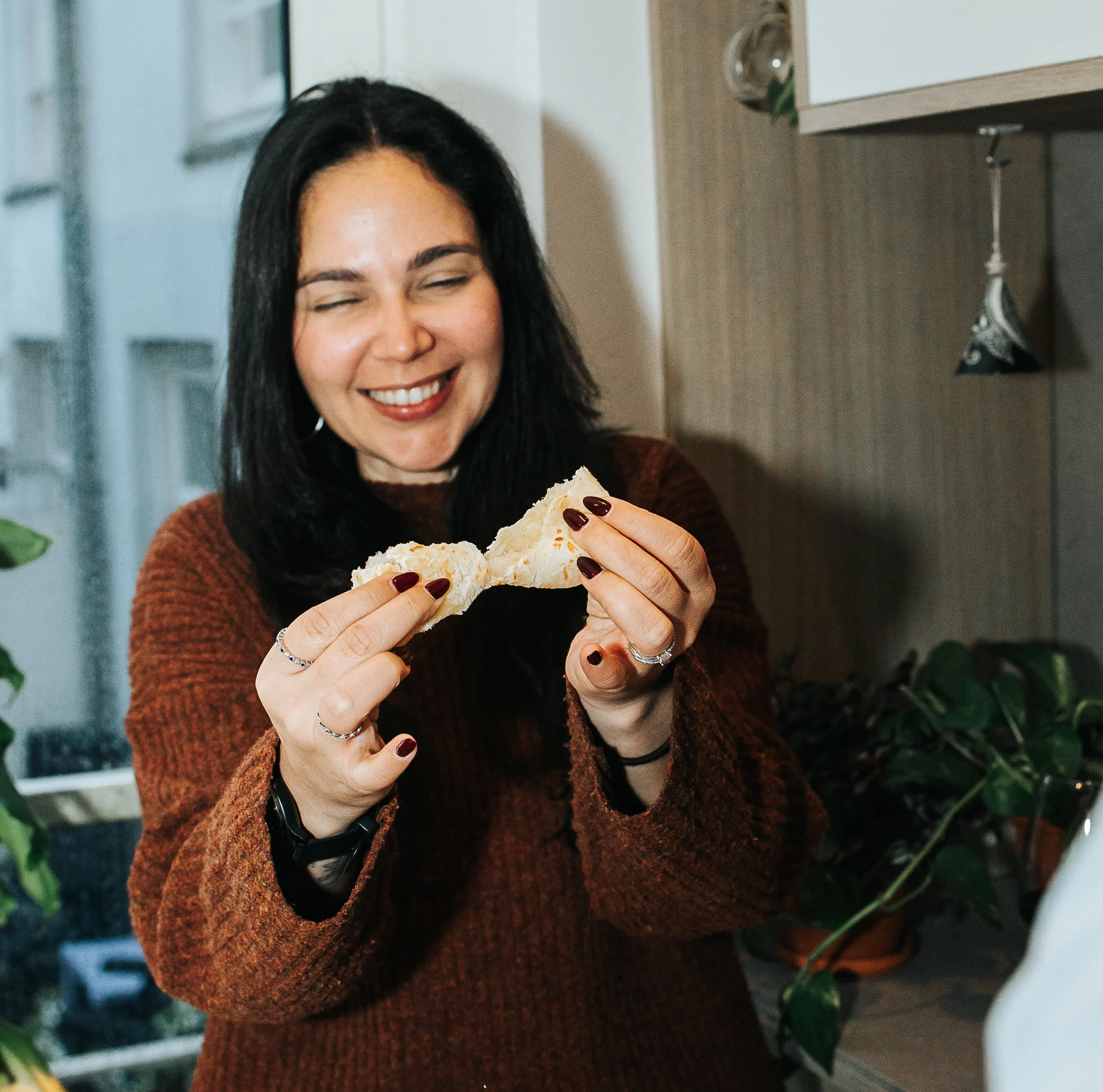 A woman pulling apart freshly baked pão de queijo before eating it.