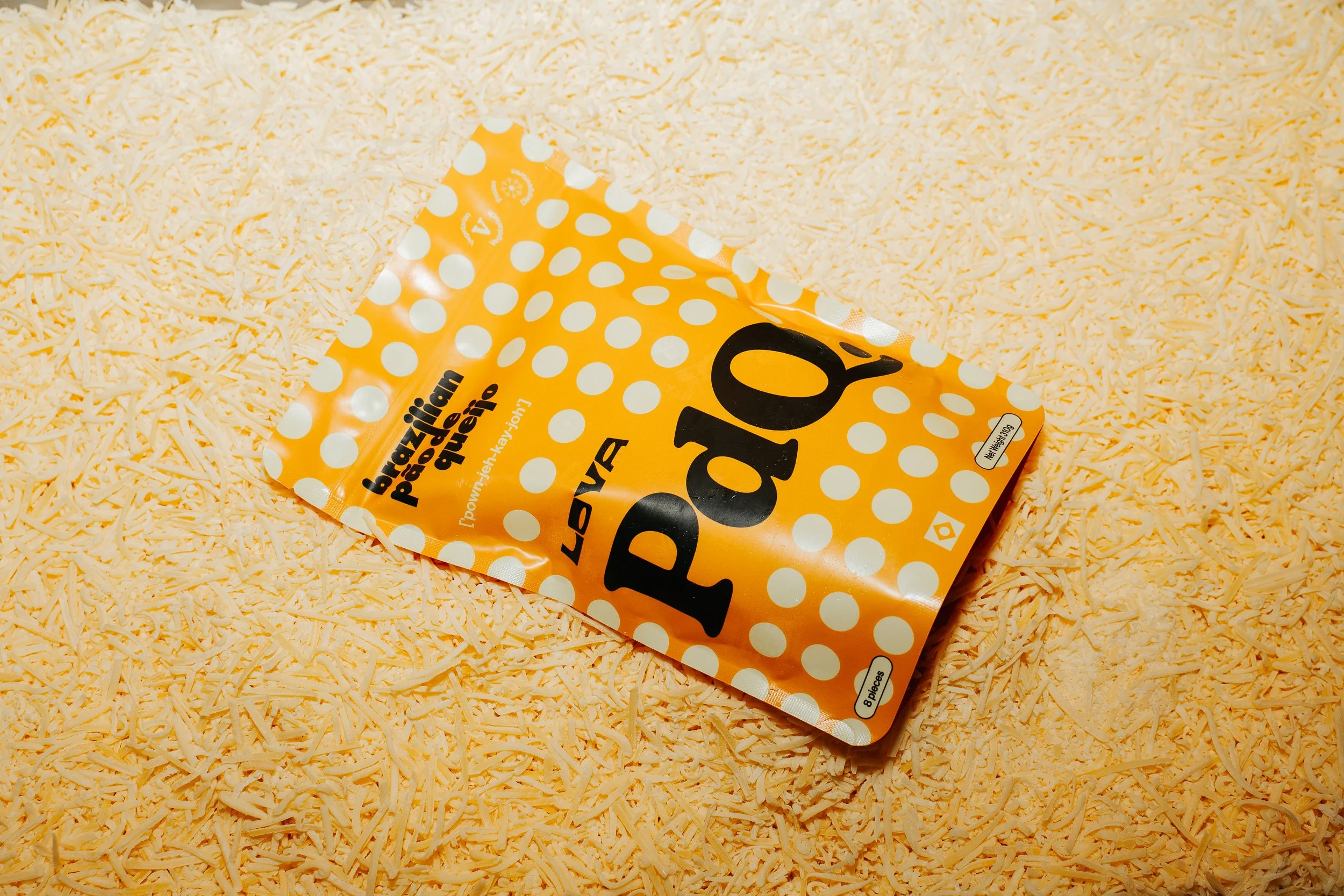 A photo of a pack of Lova's frozen, bake at home pão de queijo package, resting on top of grated cheese ingredients.