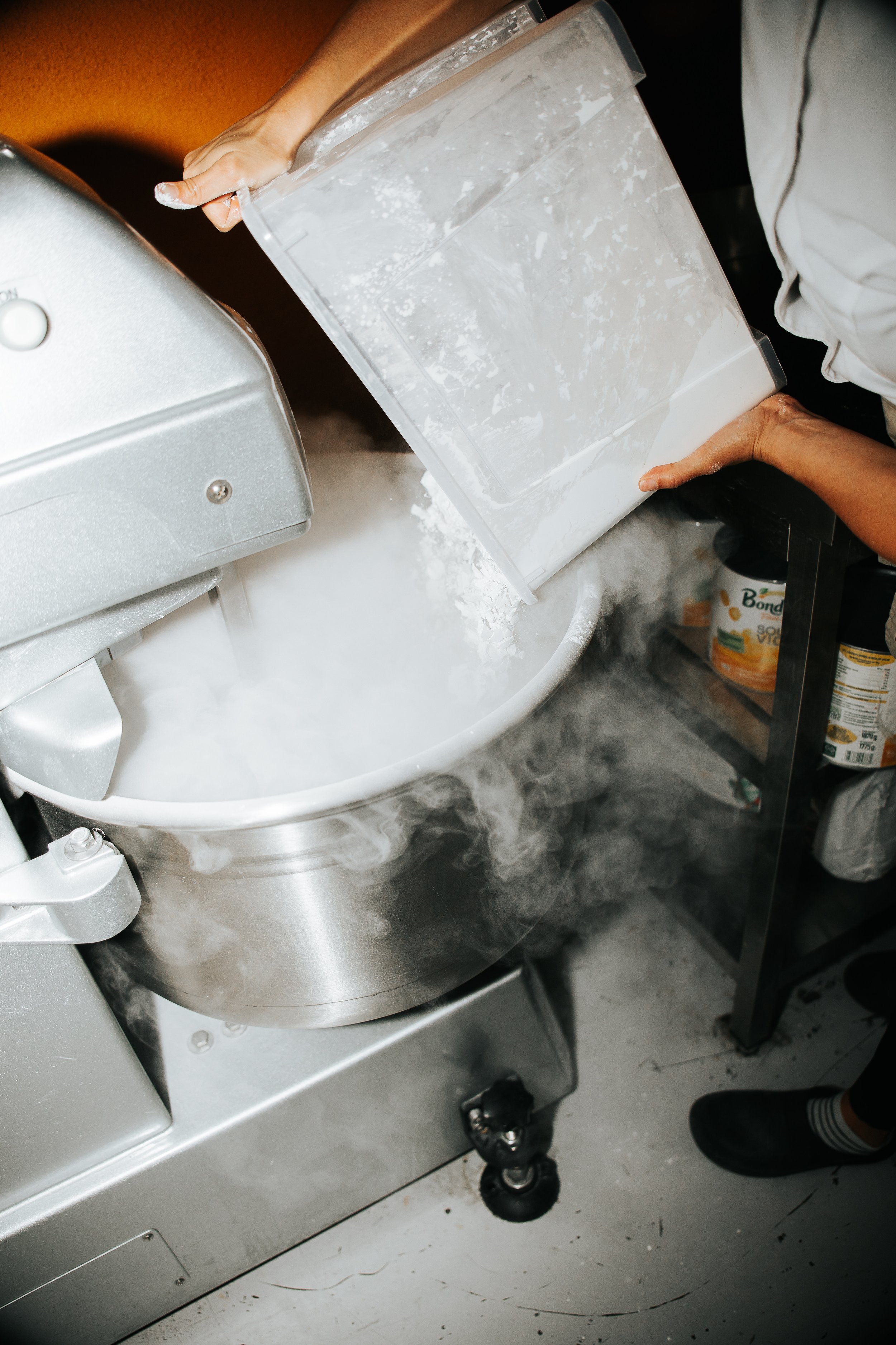 A person adding flour to a mixer, in the process of making pão de queijo.
