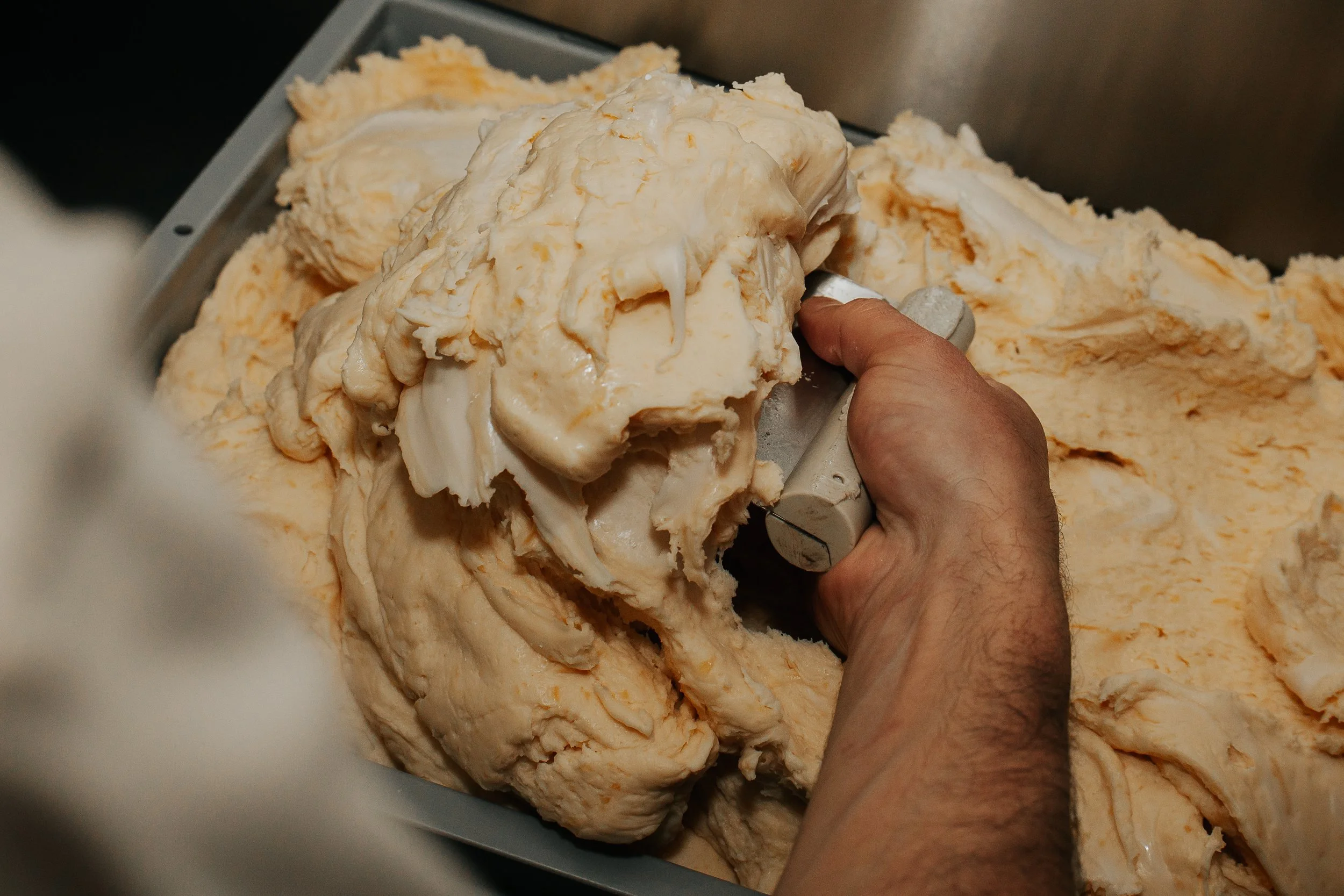 Hands scooping up pão de queijo dough before rolling.