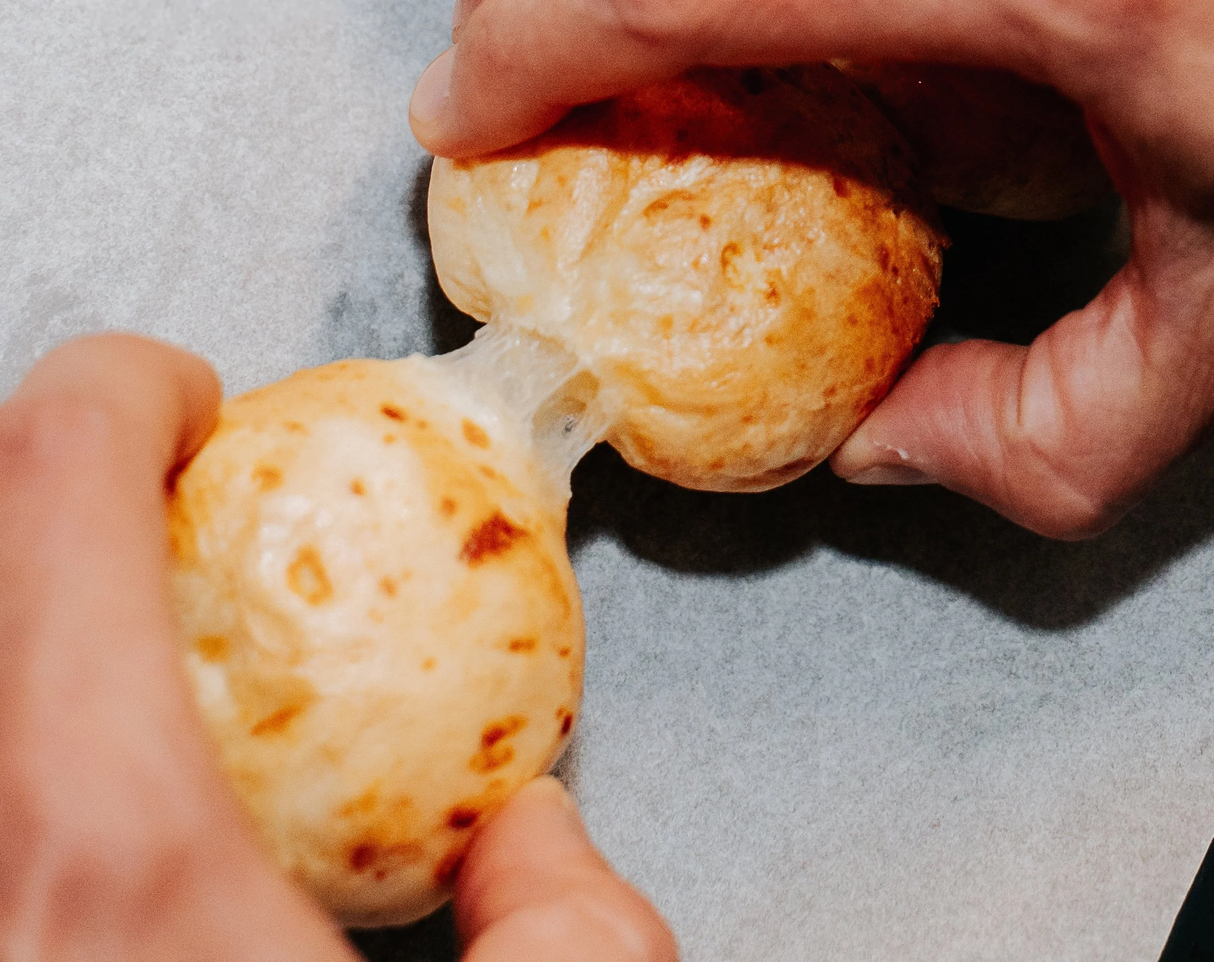 Close up photo of baked pão de queijo being pulled apart.