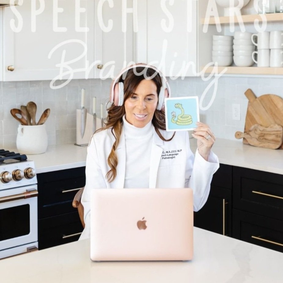 Woman in a white coat with headphones sitting at kitchen counter on a video call, holding a picture of a snake coiled around a yellow circle.