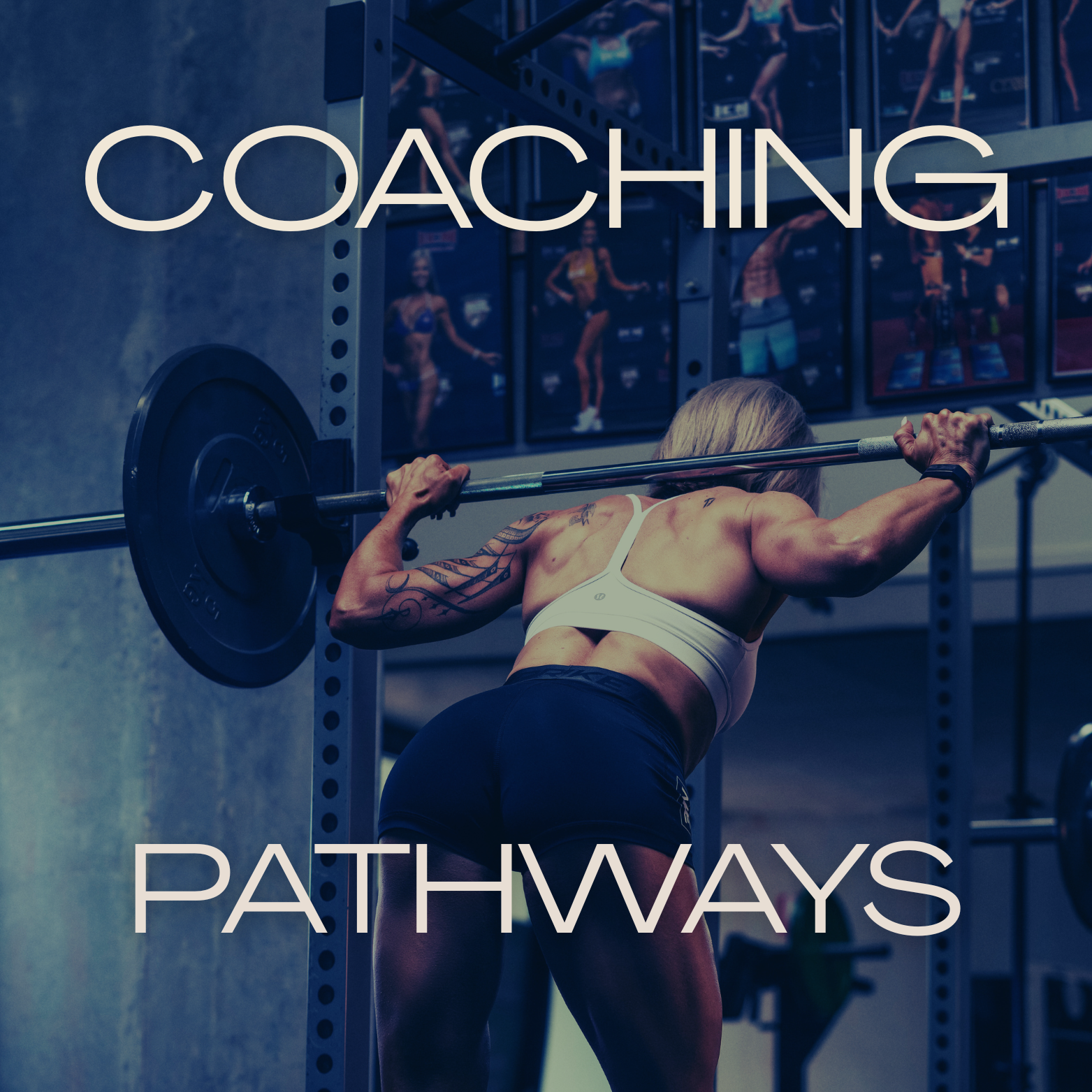 A woman with tattoos lifting a barbell in a gym, with fitness posters on the wall behind her.