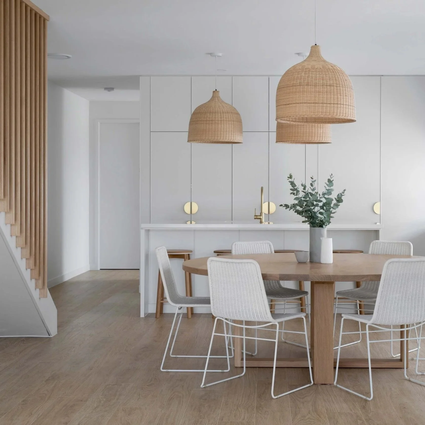 Open plan coastal style dining and kitchen with timber floors, rattan pendant lights, round timber dining table and white cabinetry — home interior design colour schemes and styling guides by Zephyr and Stone.