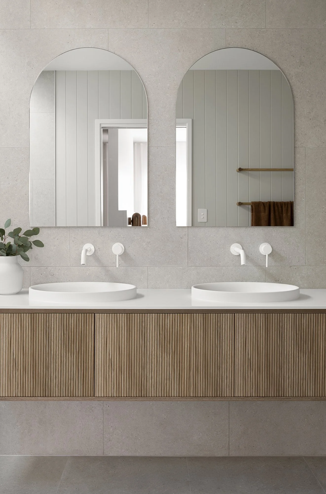 Two arched bathroom vanity mirror with with timber vanity sink and greige bathroom tiles in coral house ensuite design