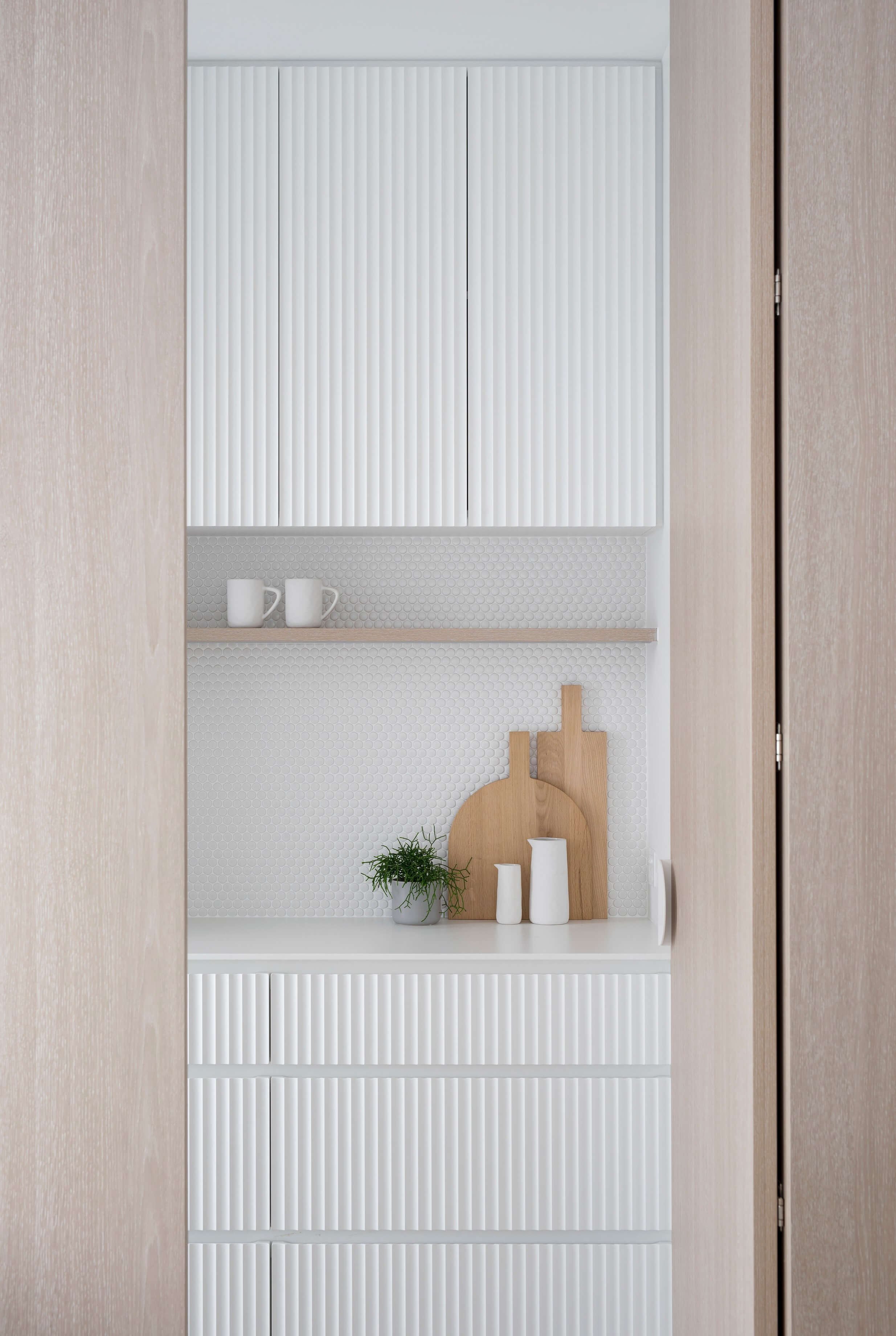 white beach kitchen design with round tiles, ribbed cabinets and wooden shelf