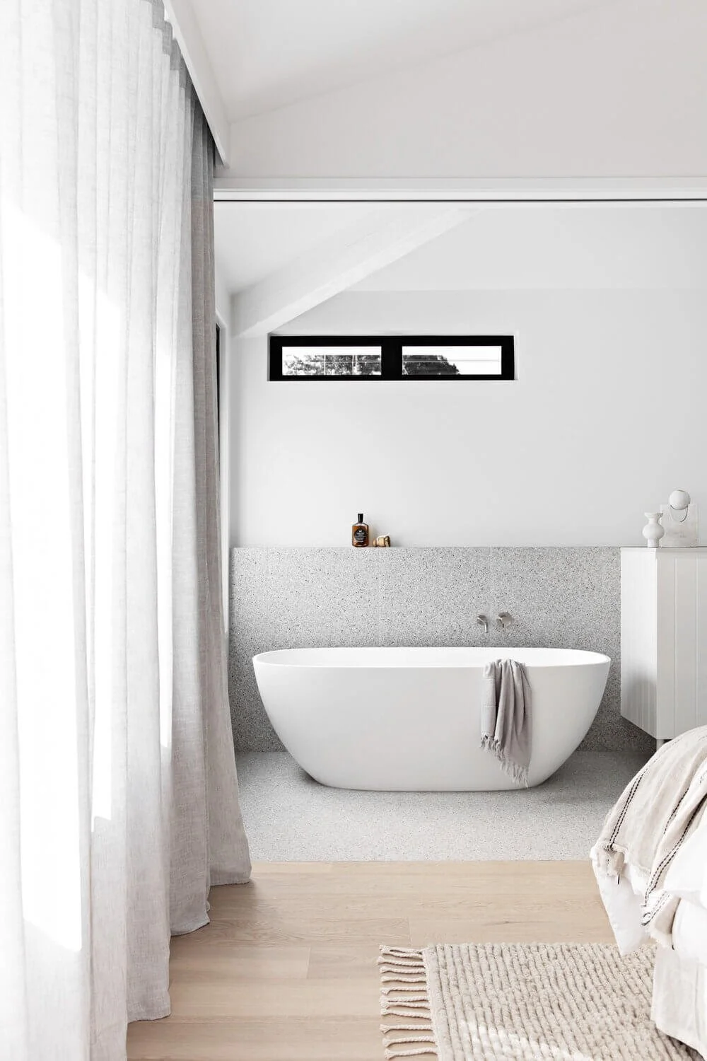 White freestanding bathtub with grey bathroom tiles and shower shelf