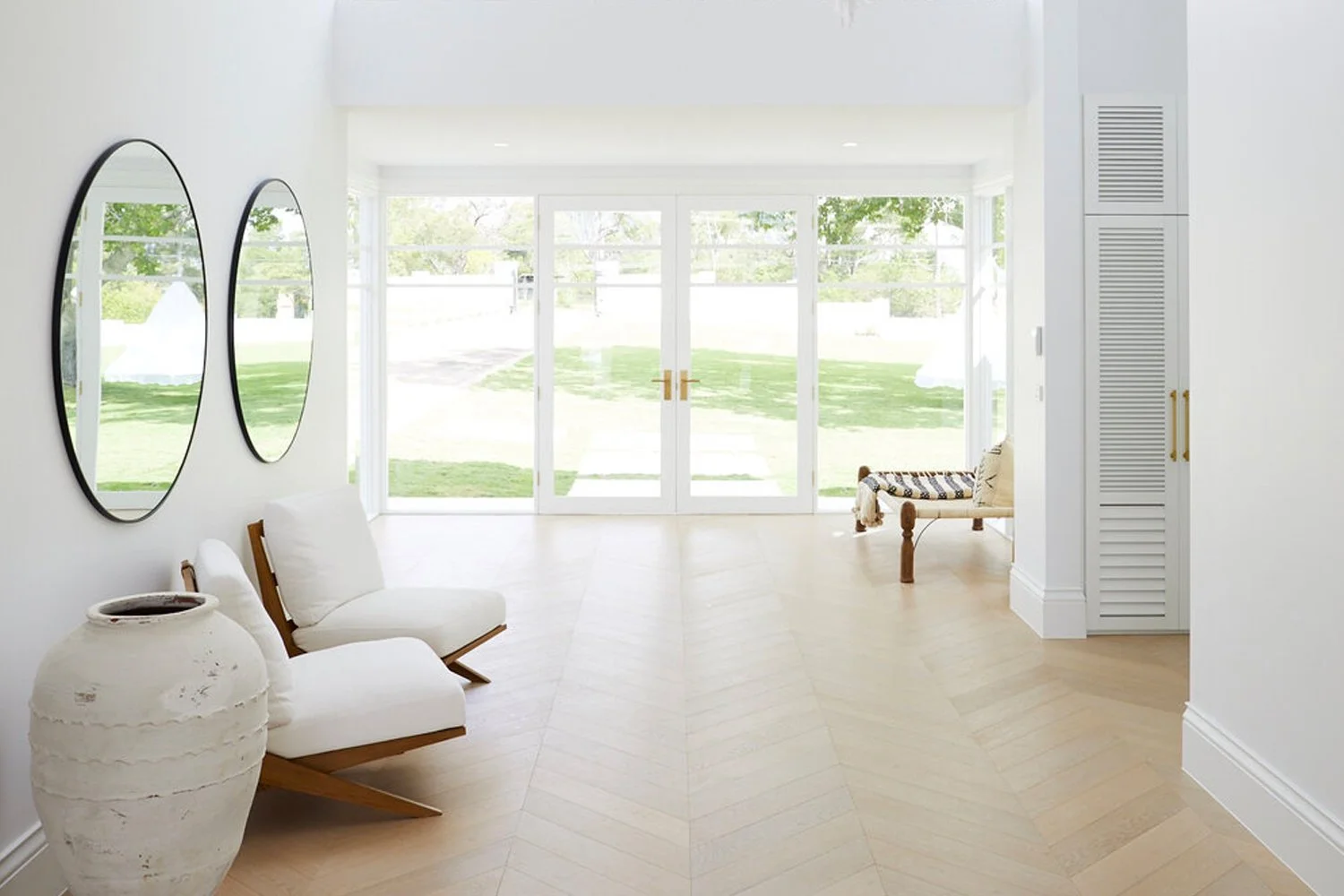 Wide entry hall around 2 metres across with double glass entry doors, side glass panels, chevron timber flooring and space for chairs either side