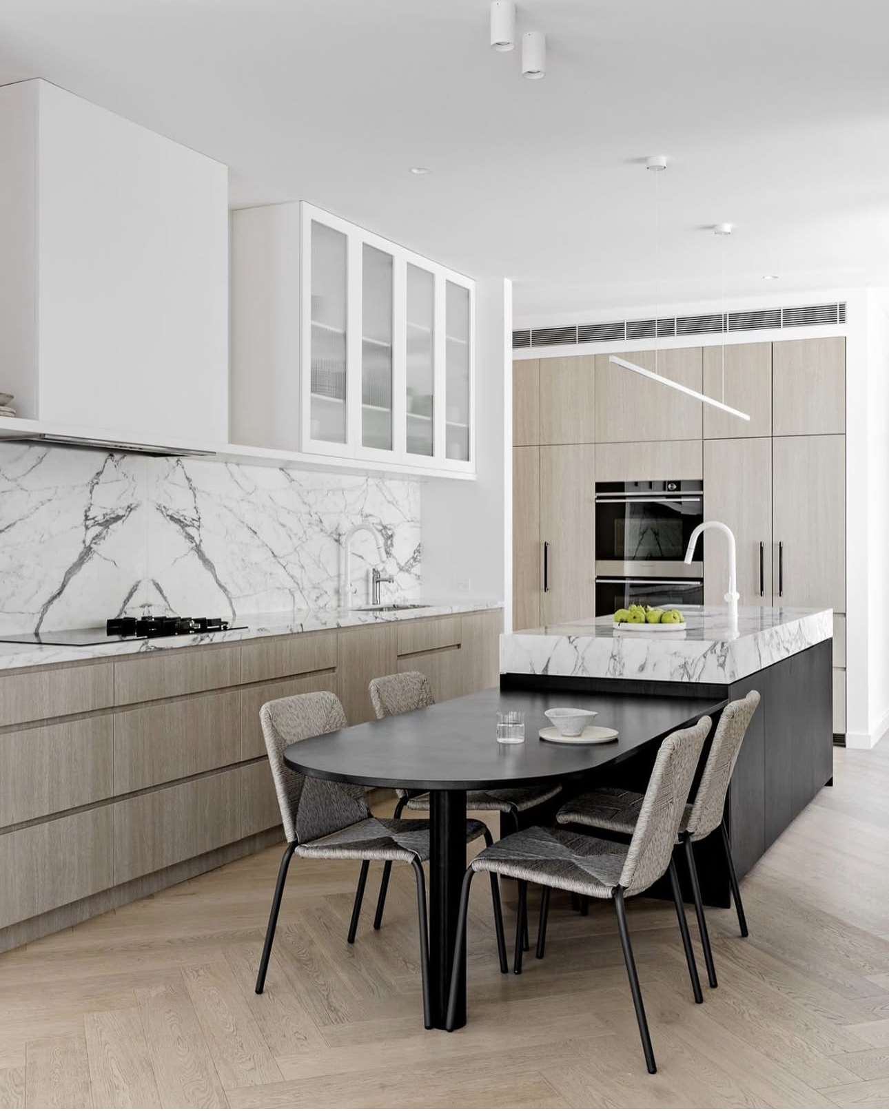 Black dining table attached to the end of a marble kitchen island bench with four dining chairs