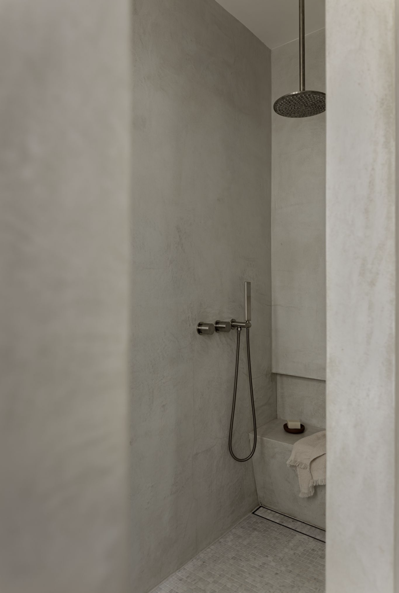 Microcement walk-in shower with a built-in bench and a ceiling-mounted rain shower head.