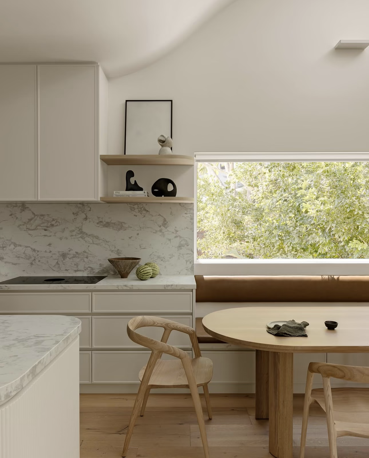 Kitchen banquette seating built in beside a window, with a timber dining table, next to the cooktop.
