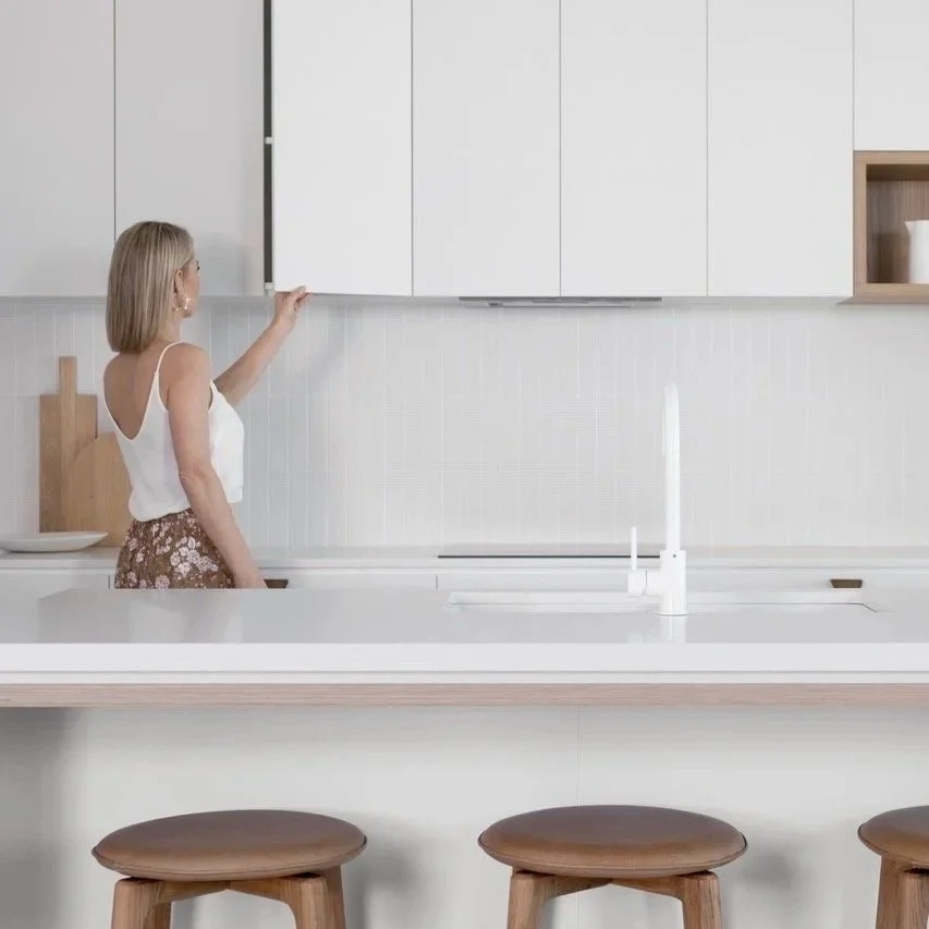 White handleless kitchen with timber accents, large island bench, vertical tile splashback and integrated appliances — minimal and functional kitchen design by Zephyr and Stone.