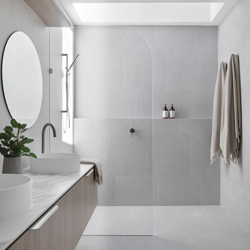 Grey stone bathroom with arched shower feature, round mirror, marble vanity top, vessel sink and natural skylight — minimal and timeless bathroom design by Zephyr and Stone.