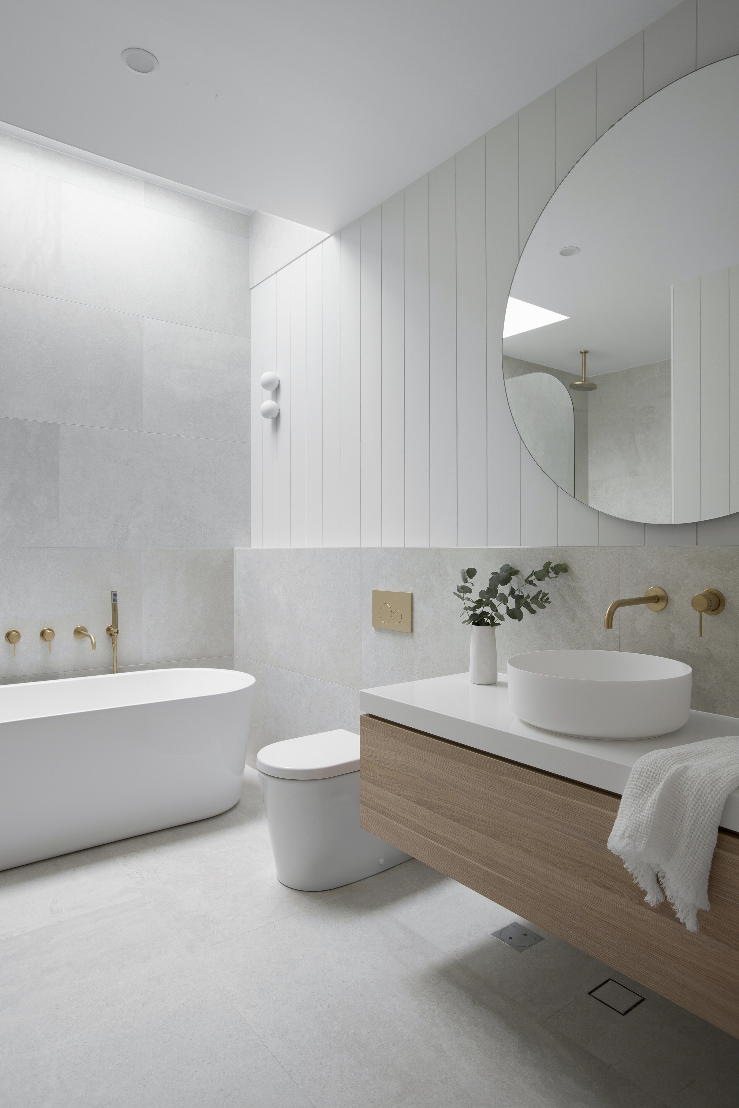 Classic coastal bathroom design with grey bathroom tiles and round bathroom vanity mirror and wall paneling