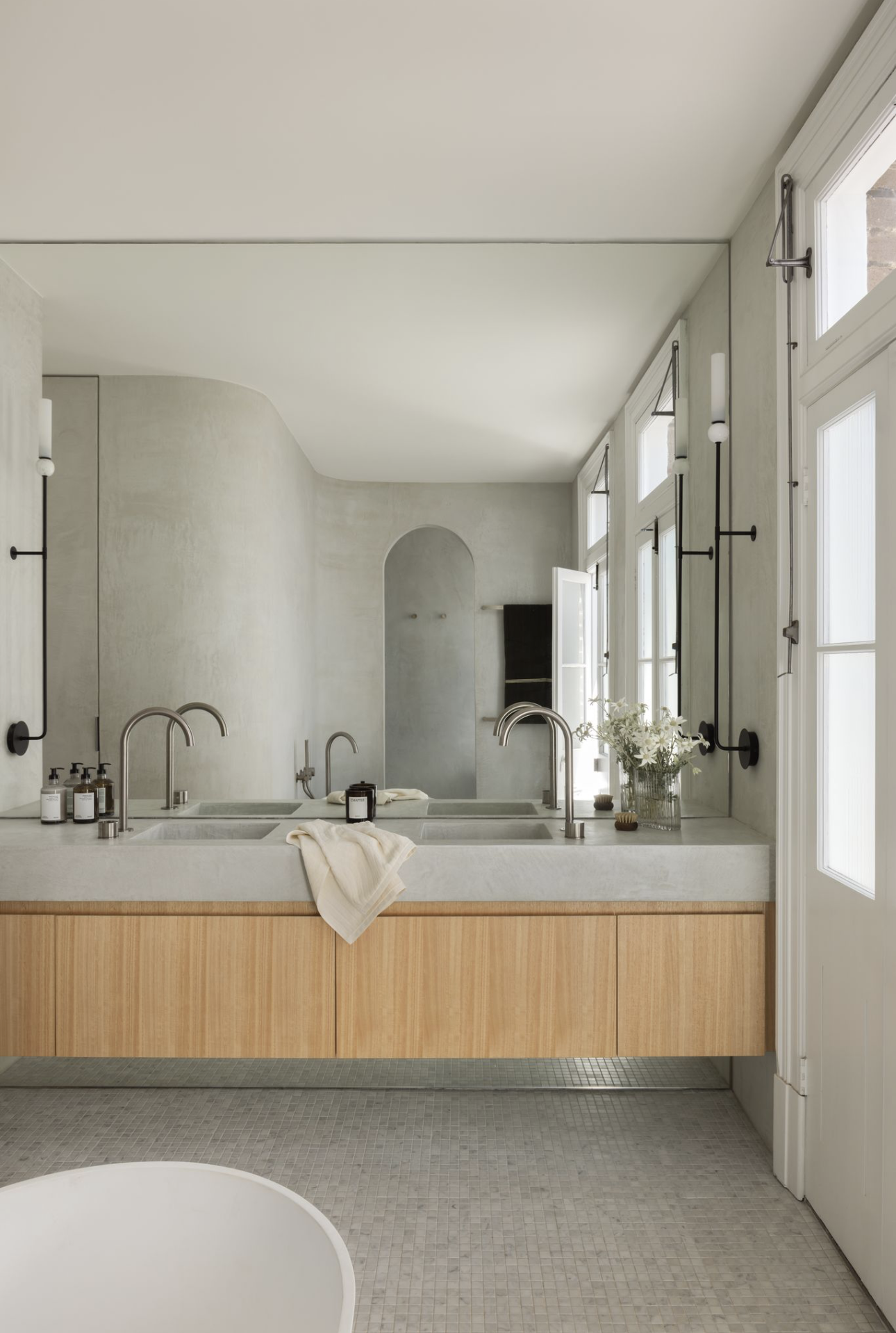 Double timber vanity in a microcement bathroom, with a curved wall and arched opening reflected in the mirror.
