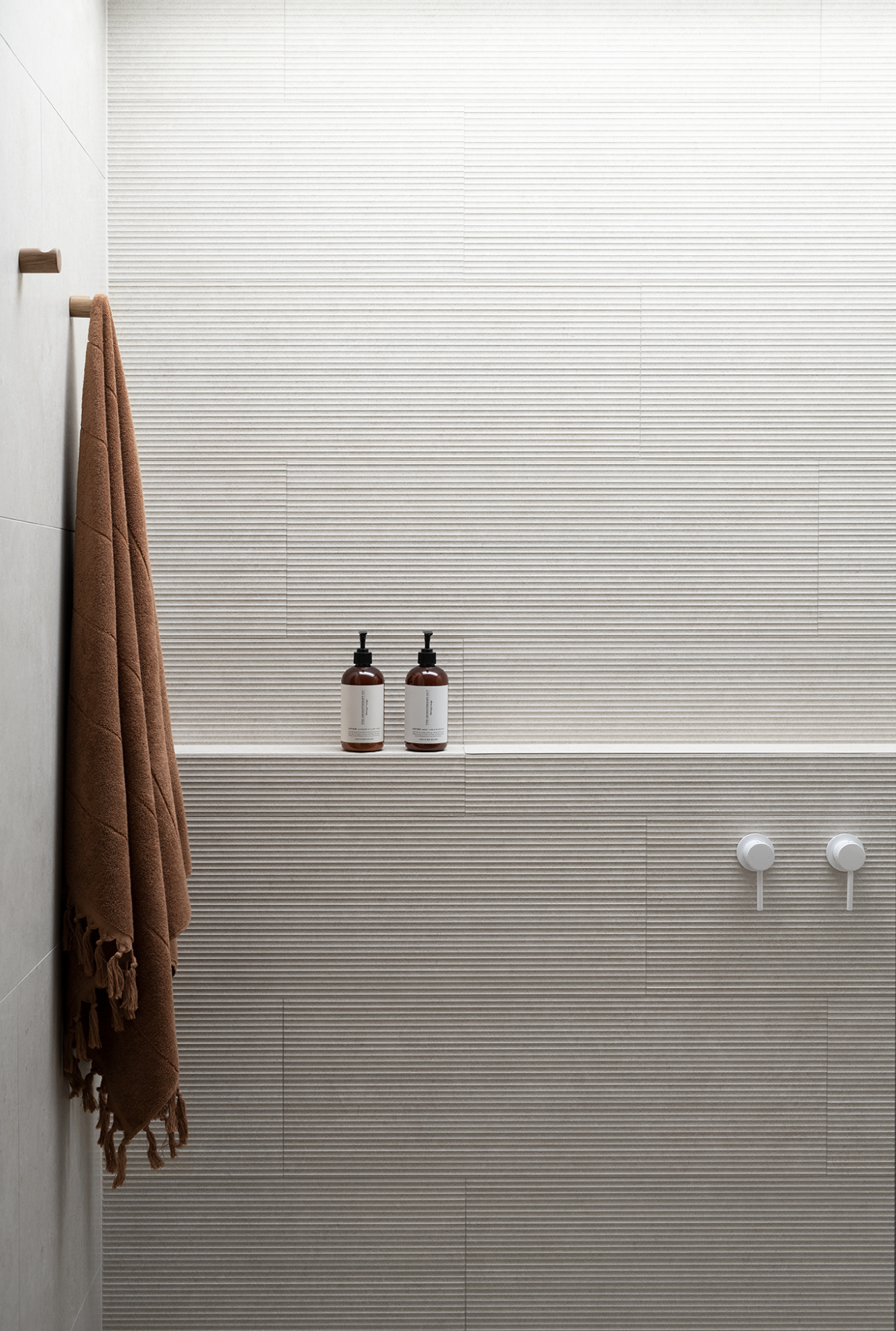 A coastal minimalist ensuite shower featuring ribbed stone tiles, soft tan towel and white bathroom tapware — bathroom design inspiration from Zephyr and Stone.