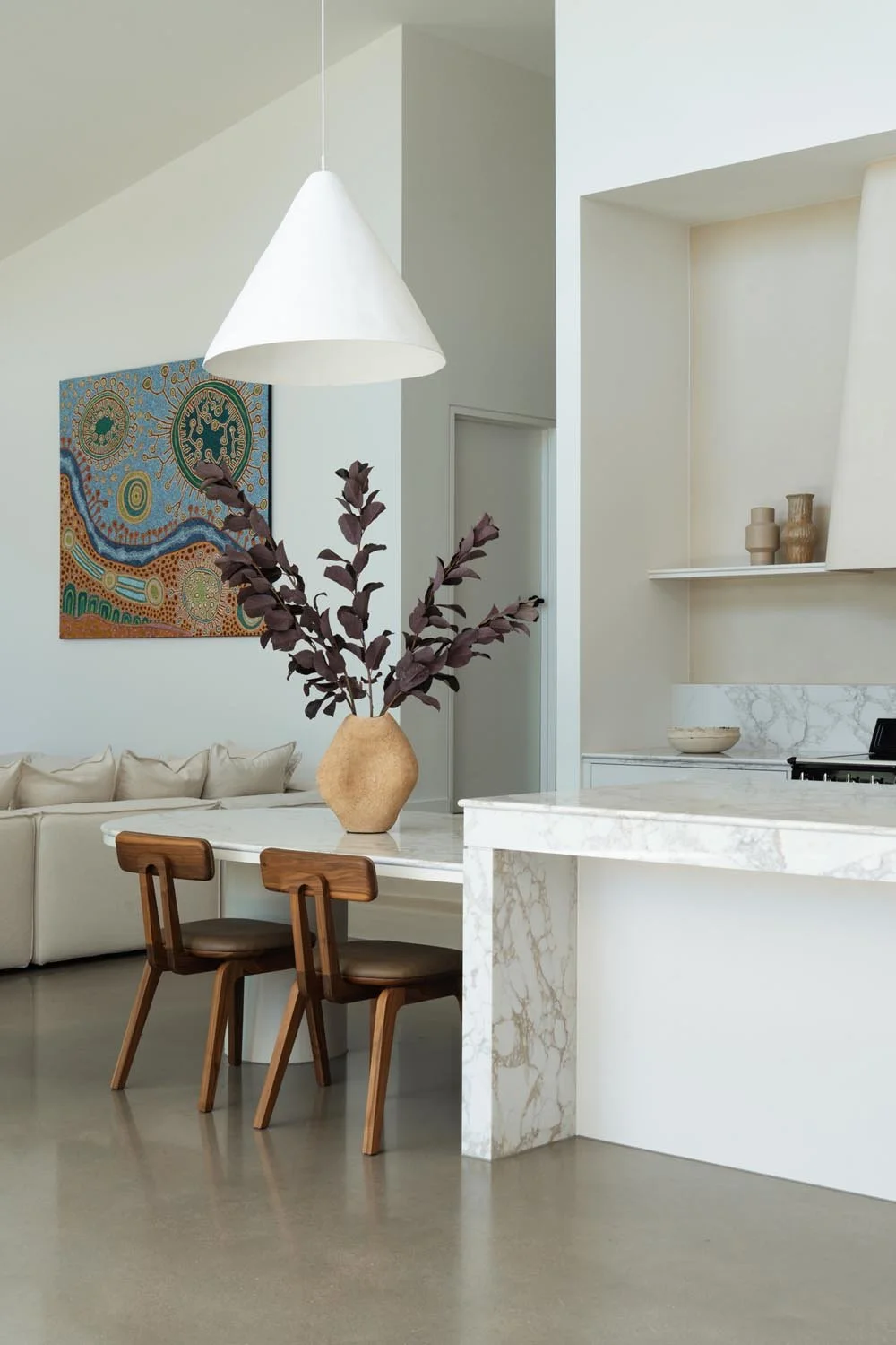 White stone kitchen island bench with a dropped dining section and timber dining chairs