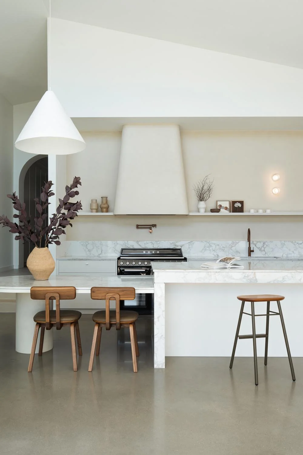 White stone kitchen island bench with a dropped dining section at one end and timber dining chairs