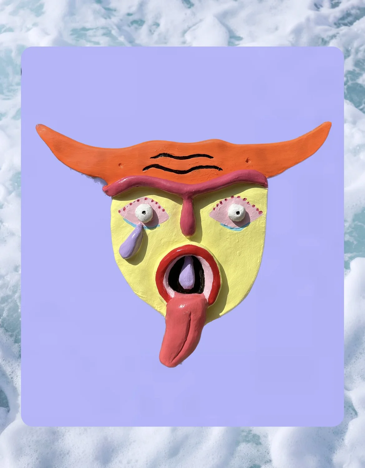 Colorful mask with exaggerated facial features, including a yellow face, pink eyebrows, orange horns, and a tongue sticking out, set against a light blue background with water textures.