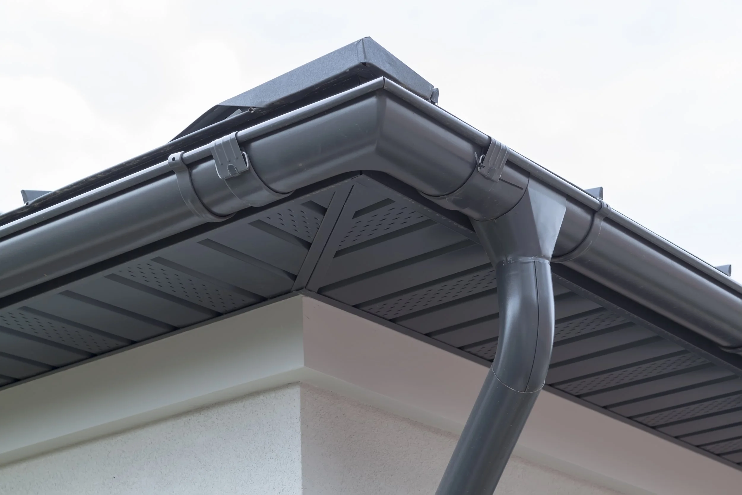 Close-up of a house corner showing gutter, downspout, roofline, and soffit with vented panels.
