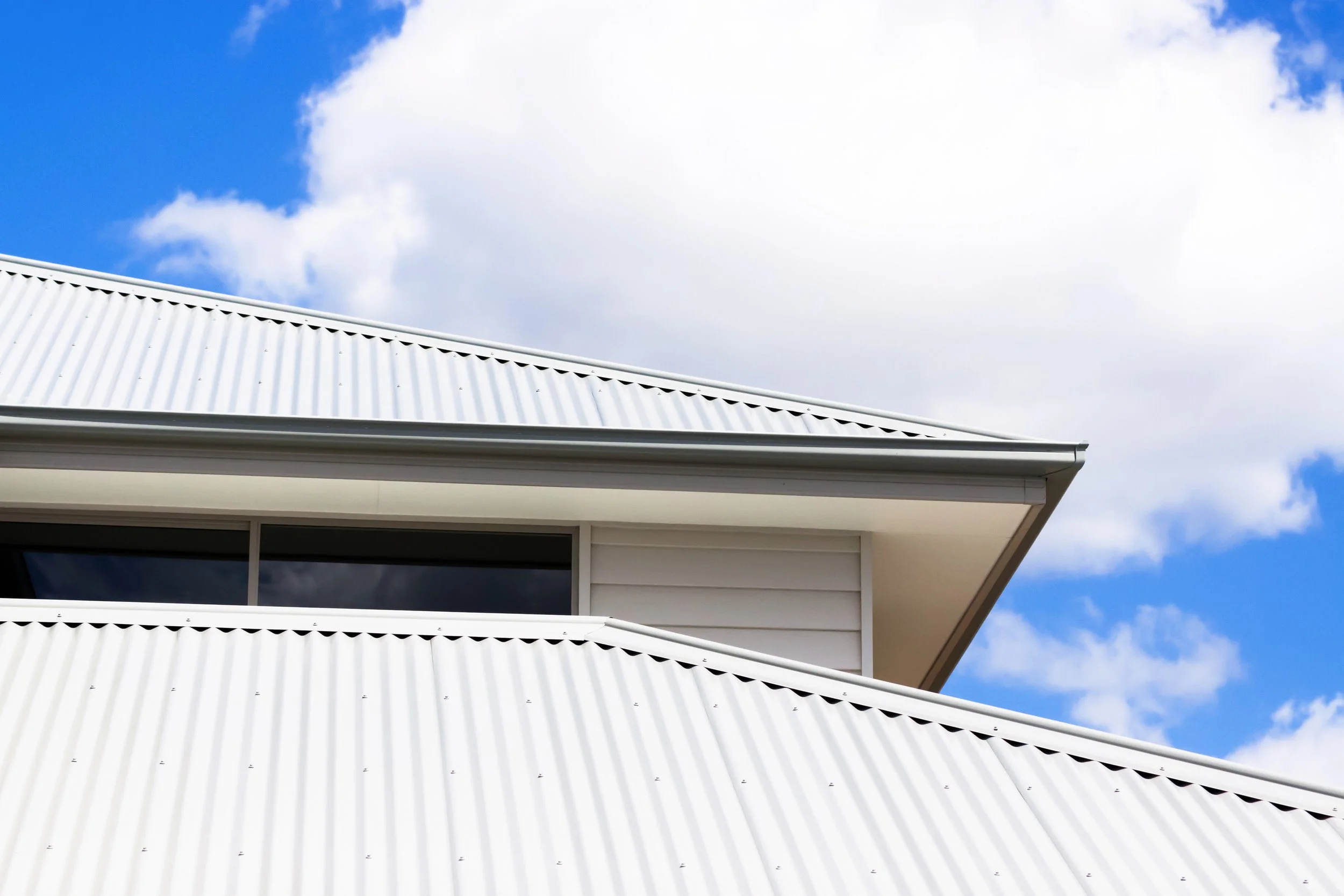 Close-up of a modern building's white metal roof with a cloudy blue sky in the background.