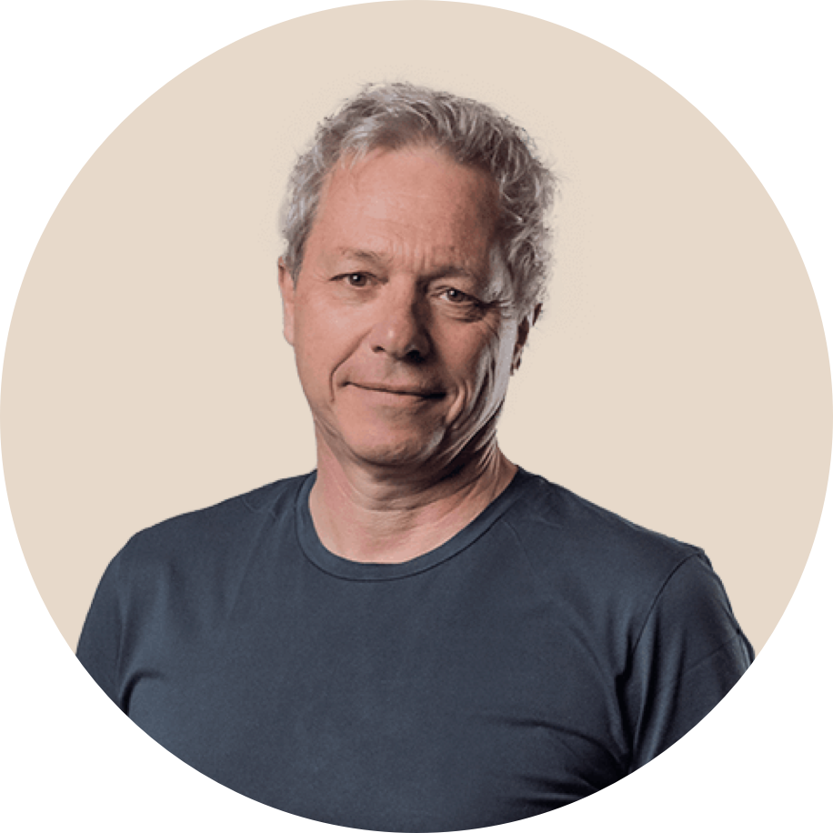 Ein Mann mit grauem, lockigem Haar trägt ein schwarzes T-Shirt und lächelt leicht.