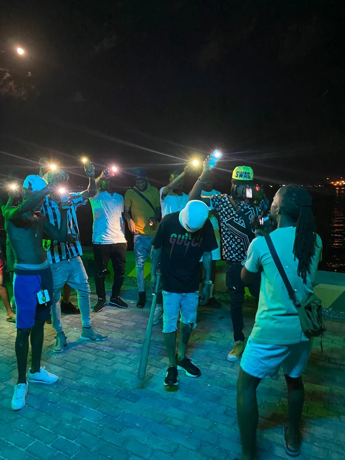 A group of young people on a boat at night, holding flashlights and socializing by the water.