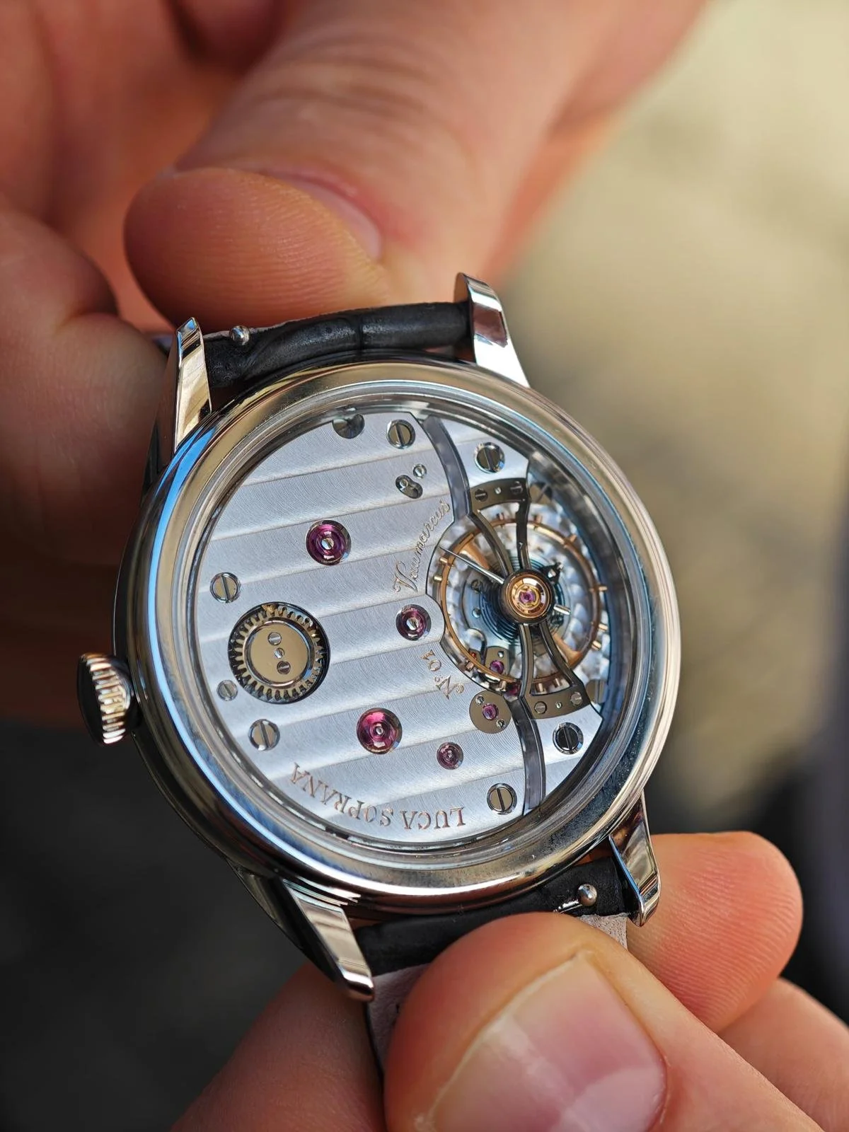Close-up of a luxury mechanical watch with a transparent dial showing its intricate inner gears and mechanisms, labeled "L.U.C. SOPRANIA" and "FRANC".